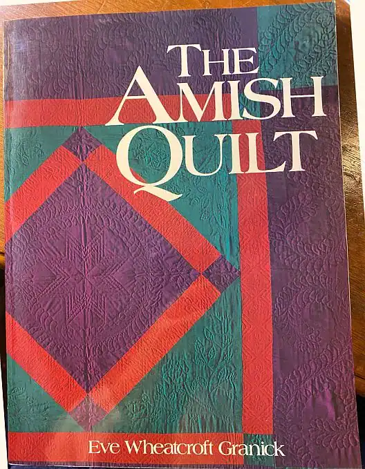 Book cover titled The Amish Quilt by Eve Wheatcroft Granick, featuring a quilted pattern in purple, teal, and red colors.