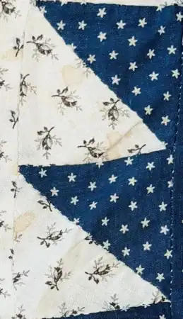 Close-up of a quilt featuring a blue fabric with white stars reminiscent of 1876 Centennial Fabric and a white fabric with small black floral designs, sewn together in a geometric pattern.