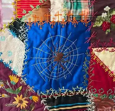 A colorful patchwork quilt with various embroidered patterns, including flowers, a spider web, and decorative stitches, on fabric pieces of different colors and textures.