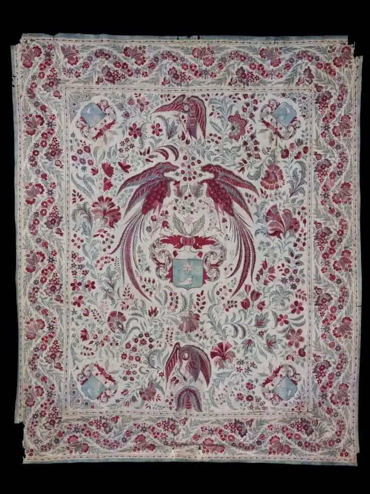 Embroidered textile with two large red birds facing each other, floral patterns, smaller birds, and four blue shields, one in each corner. The border features intertwining floral and leaf motifs.