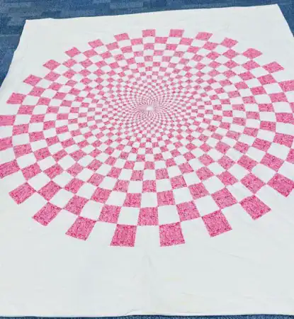 White quilt featuring a pink and white checkered circular pattern that radiates from the center.