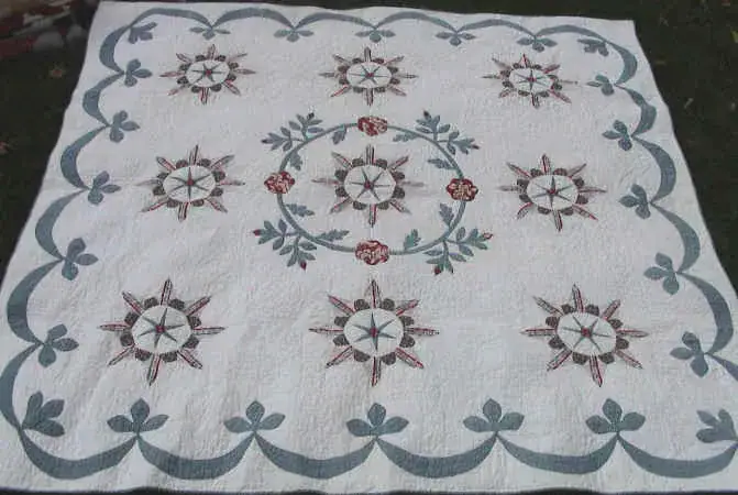 White wholecloth-style applique quilt with stars, flowers and a scalloped vine border in blue and red