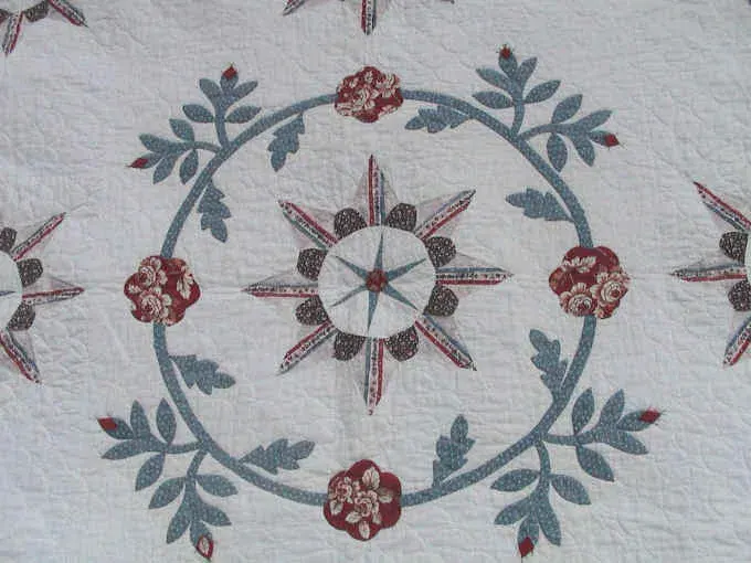 Close-up of an applique wreath of red flowers and blue leaves around a center star