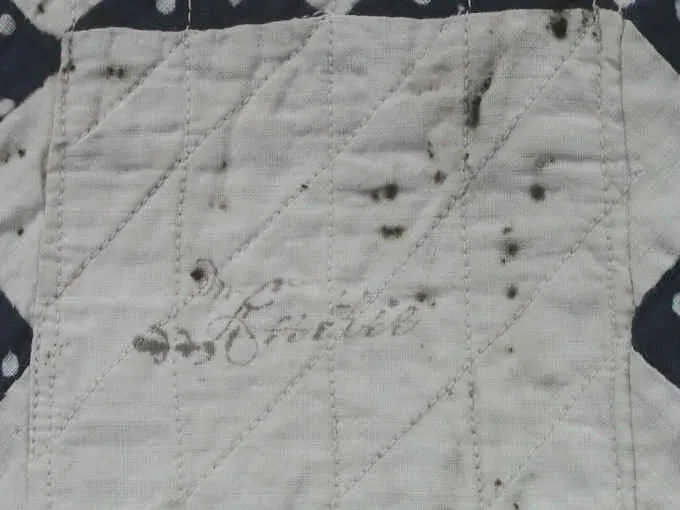 Ink name Ruthie written in a white block of the 1878 doll quilt, with small stains