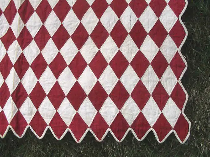 Close-up of red and white diamonds and the scalloped edge of the doll quilt